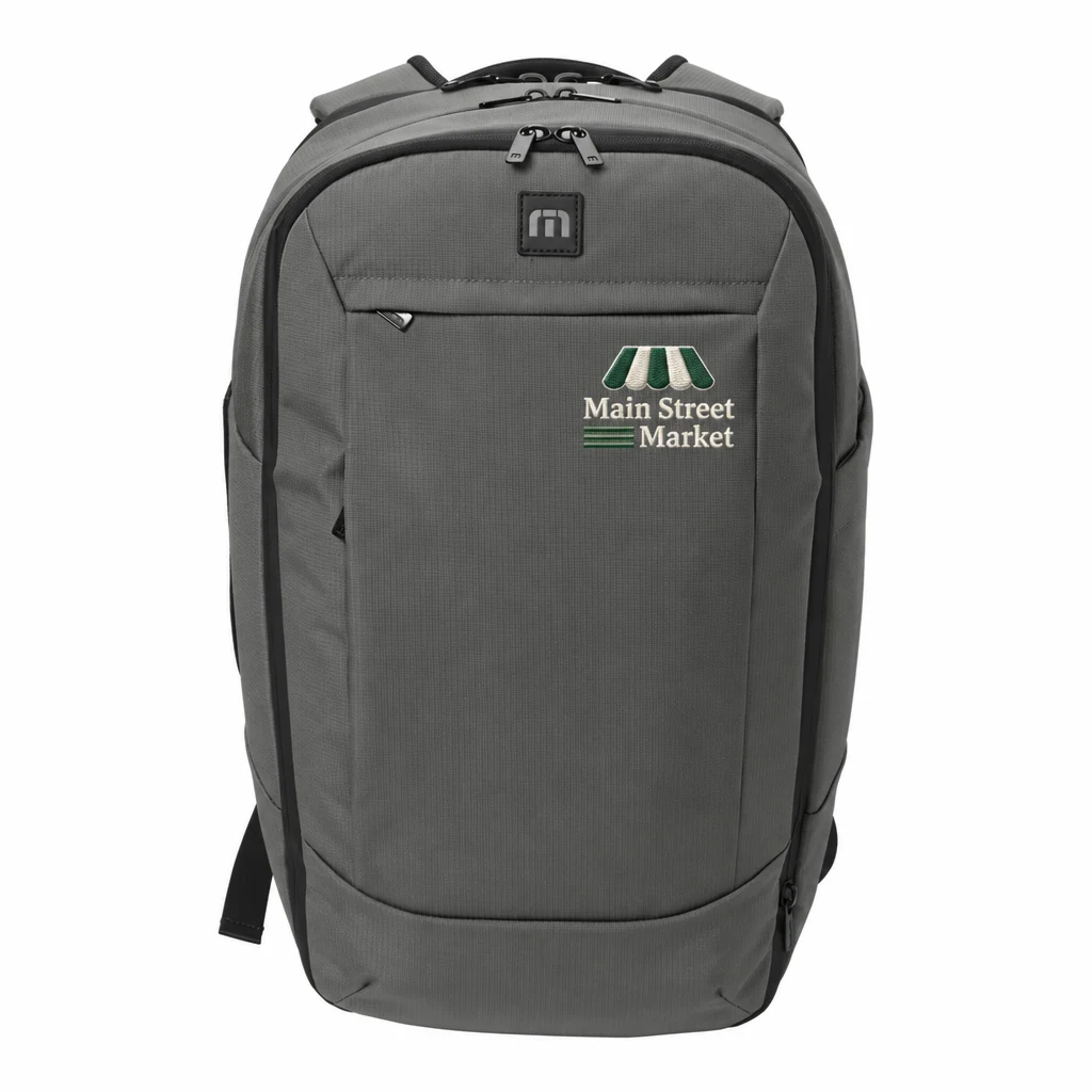 Custom TravisMathew Lateral Backpack (TMB107) in Graphite, flat-lay view with a custom embroidered logo.