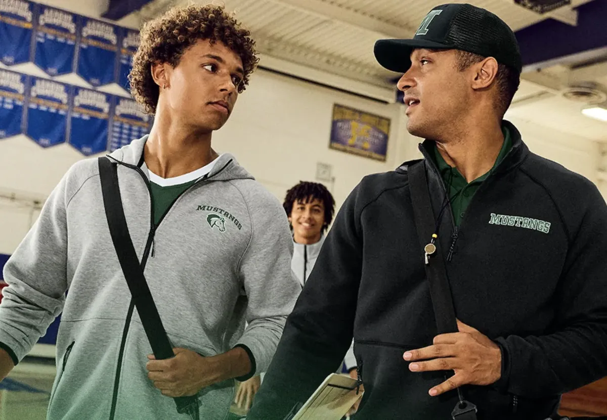 Coach and students wearing gray and black zip-up hoodies with embroidered team logos
