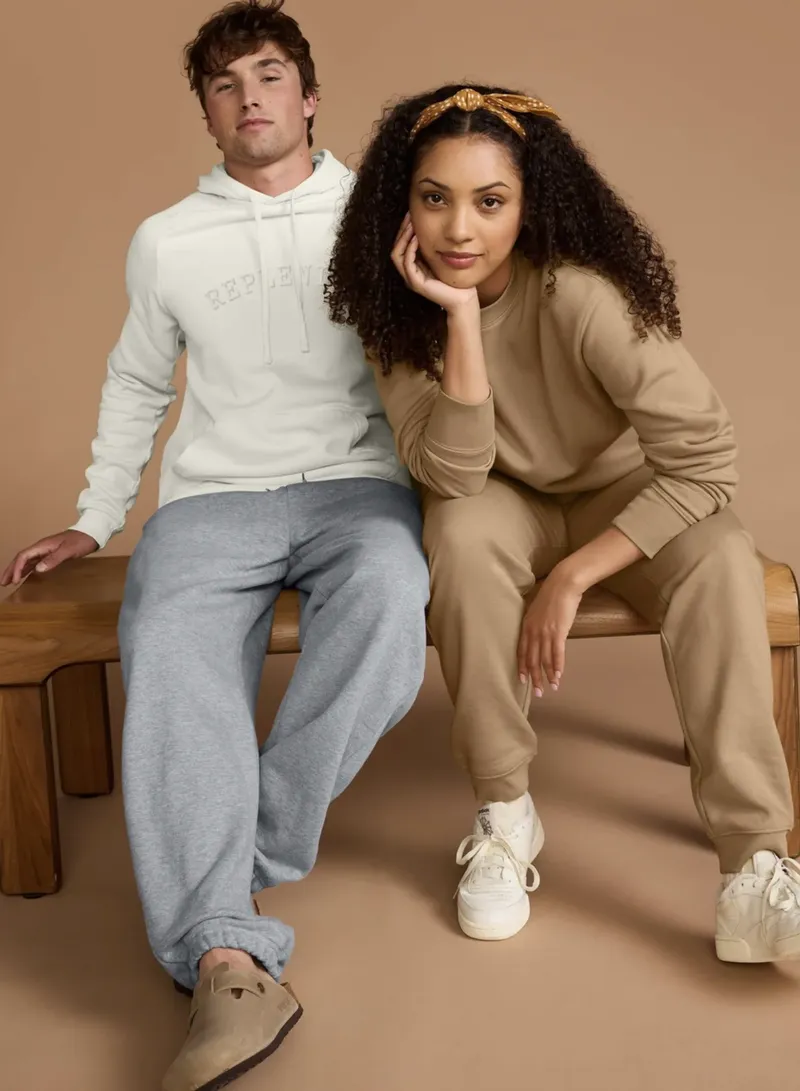 Man wearing a white pullover hoodie beside a woman wearing a tan crewneck sweatshirt and matching sweatpants