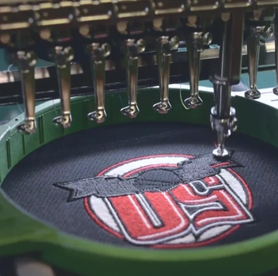 Embroidery machine stitching a red and white logo inside a green hoop in our Norfolk shop