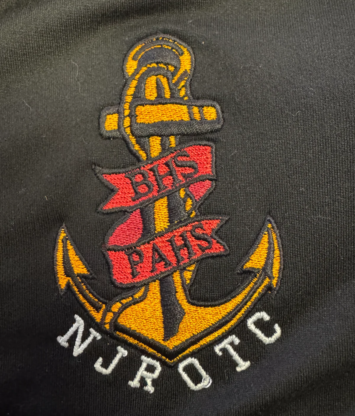 Red and gold anchor emblem with NORFOLK lettering embroidered on dark fabric