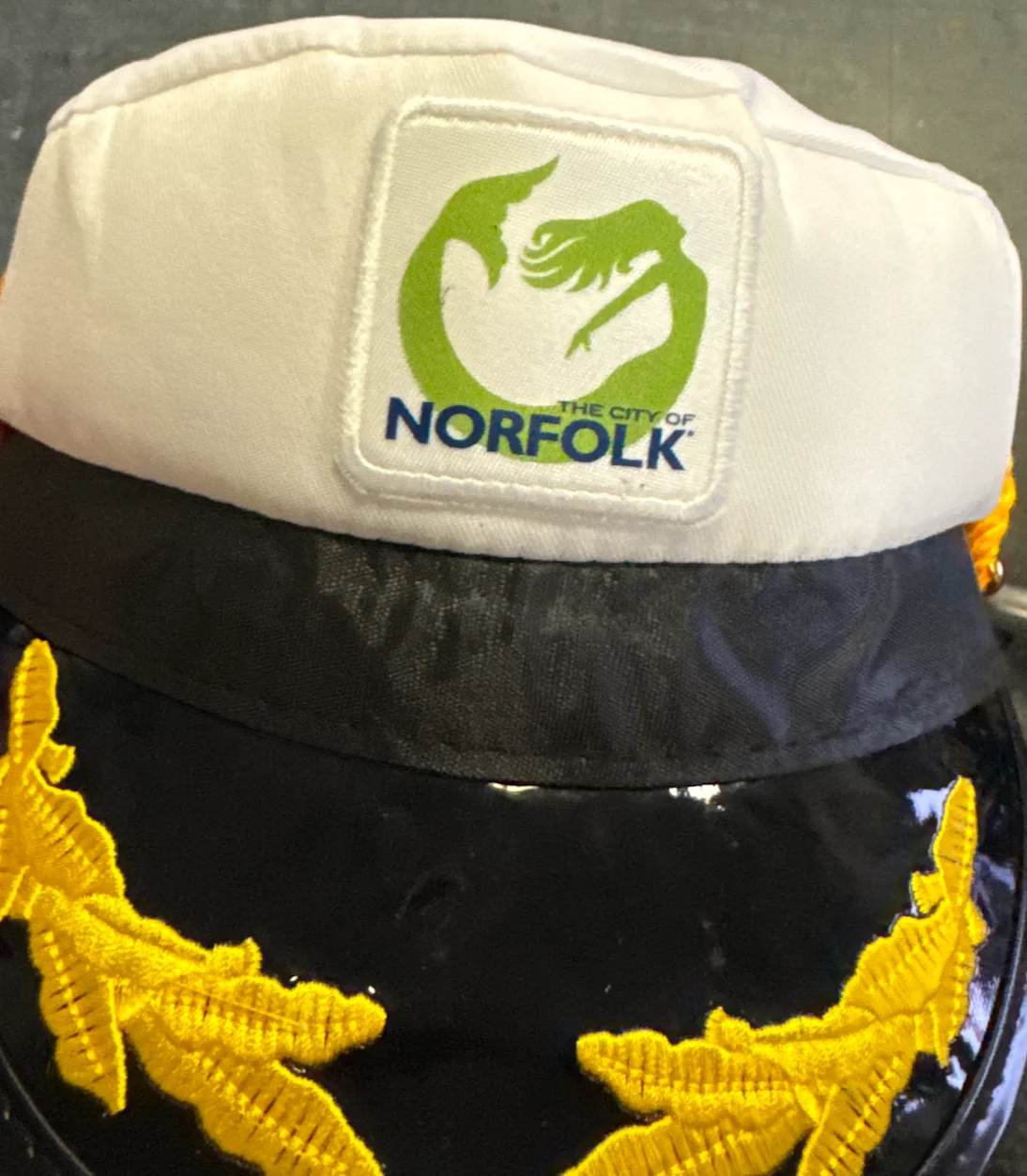 White specialty cap with a City of Norfolk embroidered patch and gold embroidery on the visor